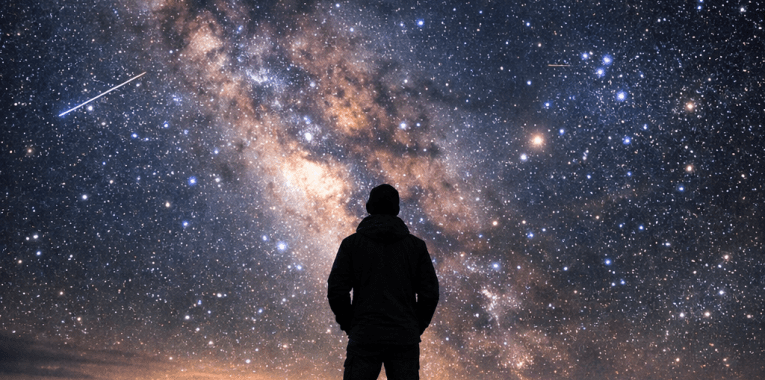 Person standing on a rocky mountain looking at the star-filled night sky with the Milky Way visible
