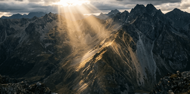 Sunlight streaming through clouds onto rocky mountain peaks and valleys
