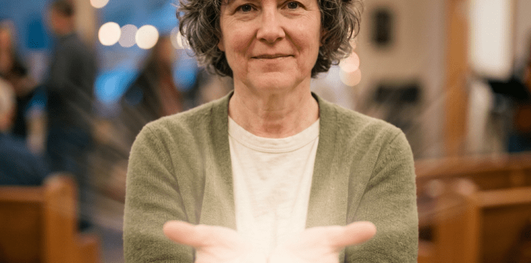 Woman with curly hair in green cardigan holding glowing light in cupped hands